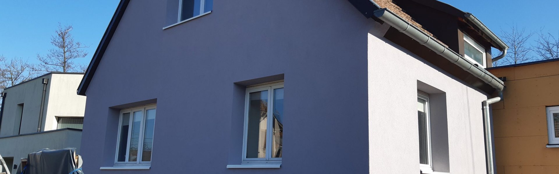 Maison rénovée avec un crépi gris-mauve moderne à Plobsheim, montrant la qualité des finitions de façade sous un ciel dégagé.