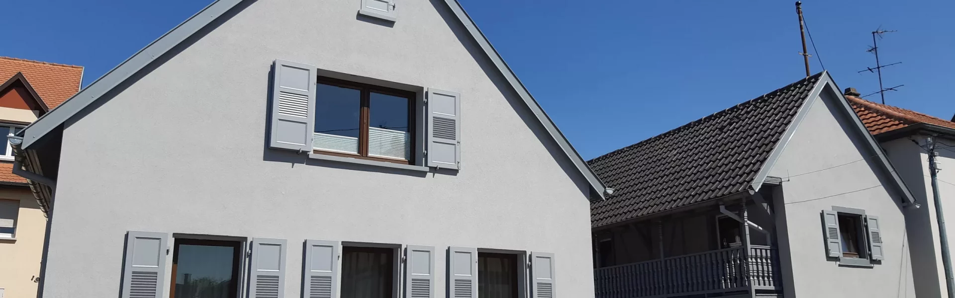 Maison rénovée avec une façade gris clair impeccable et des volets gris par SARL Acacia Aktas à Ergersheim 67120.