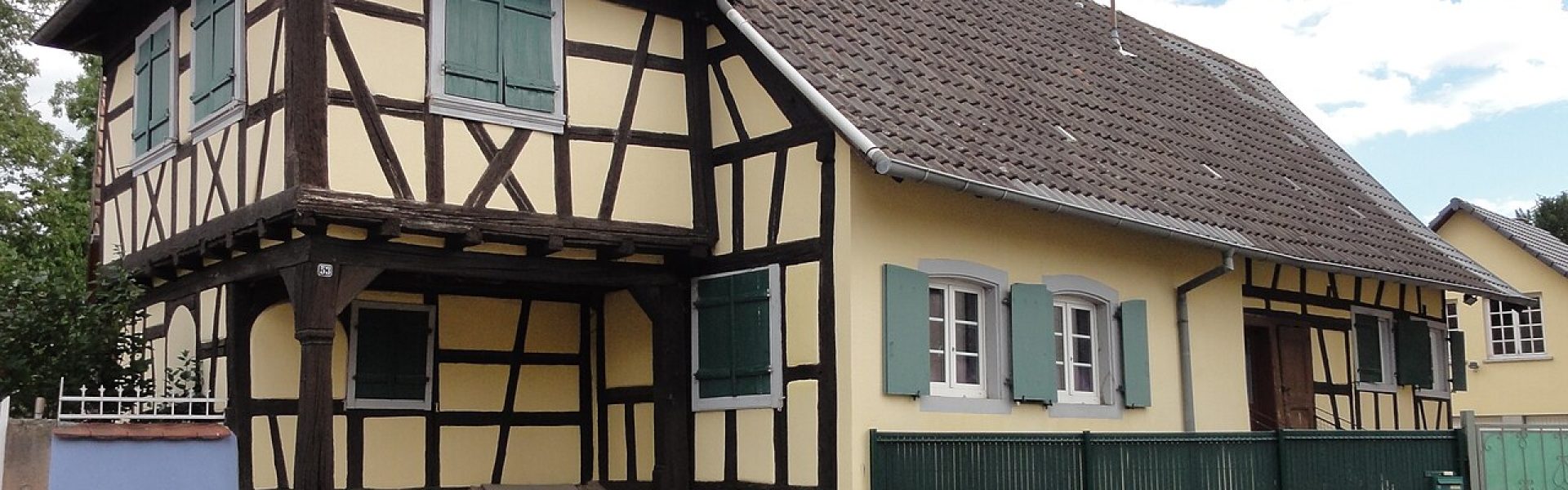 Maison alsacienne à colombages avec façade en crépi jaune et volets verts au 53 rue Principale à Niedernai.