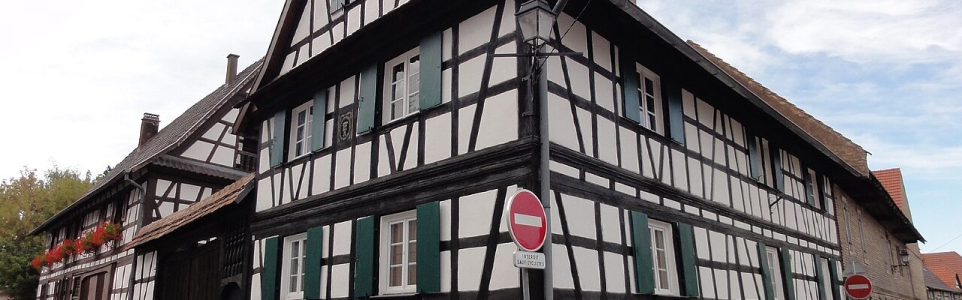 Maison alsacienne à colombages rénovée avec crépi blanc et volets verts à Vendenheim, vue d'angle rue des Bergers.