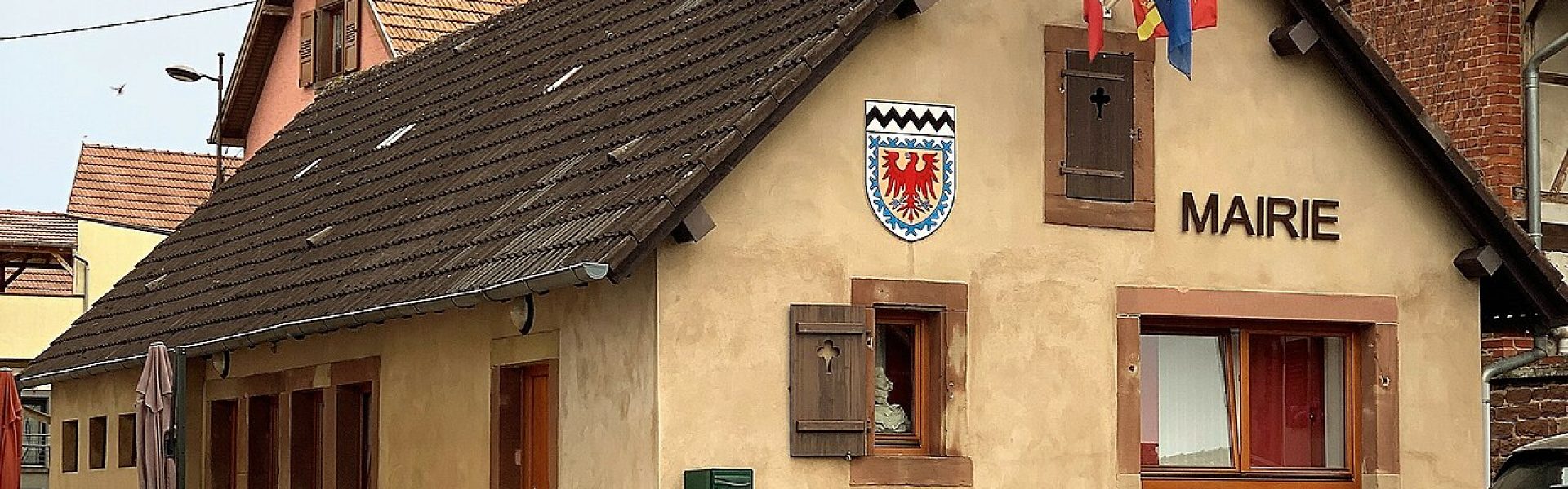 Façade rénovée de la Mairie de Wolschheim 67700, enduit de couleur ocre clair et blason communal visible.