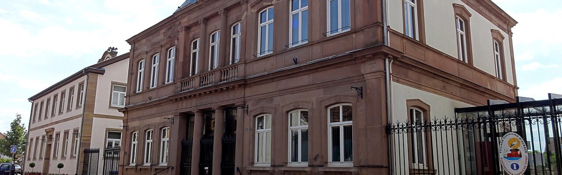 Façade monumentale de l'Hôtel de Ville de Geispolsheim en grès rouge et crépi gris avec colonnes et horloge.
