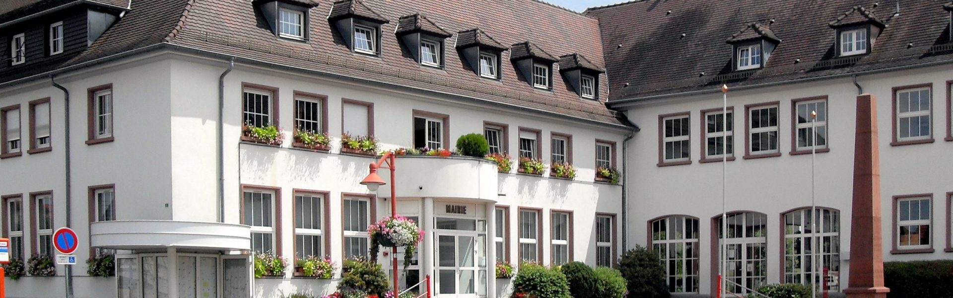 Façade blanche rénovée de la mairie d'Oberhoffen-sur-Moder avec encadrements de fenêtres bruns et toiture en tuiles foncées.